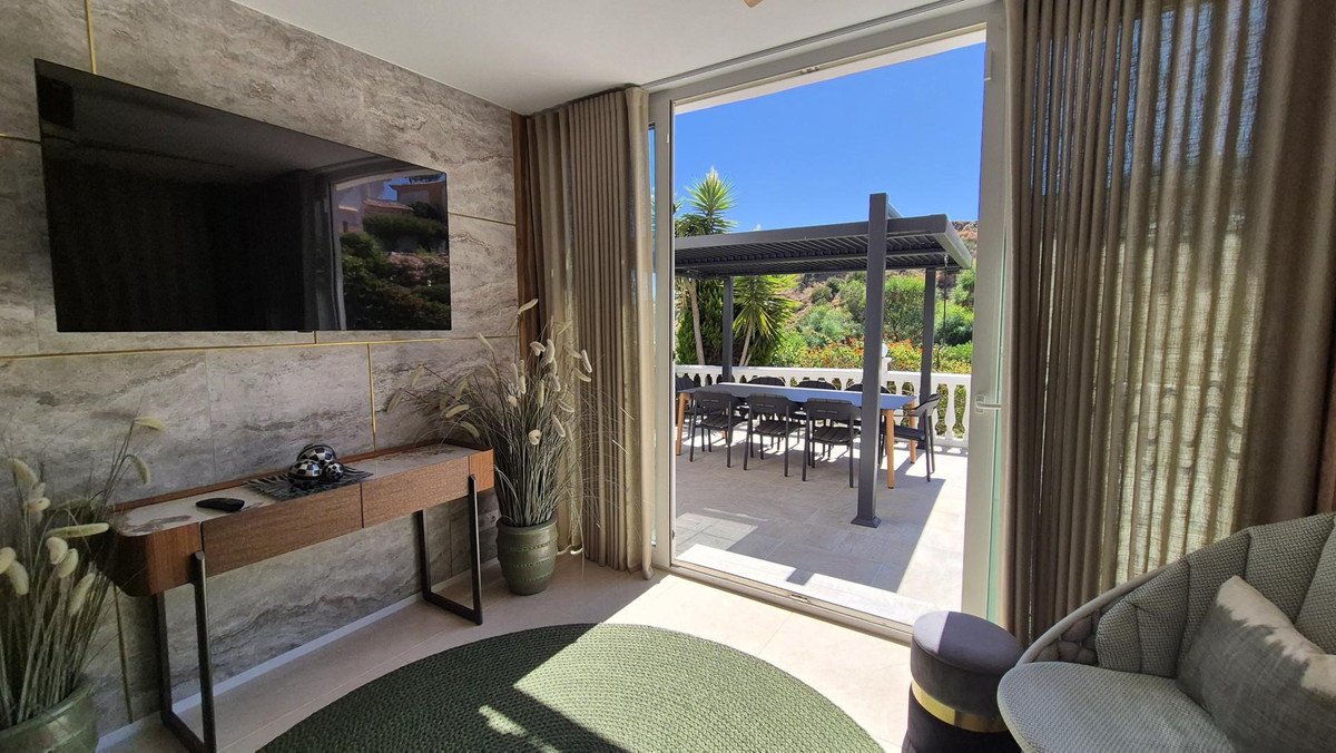 Interior view of a living area with a television and console table, looking out to an outdoor dining space with a pergola.