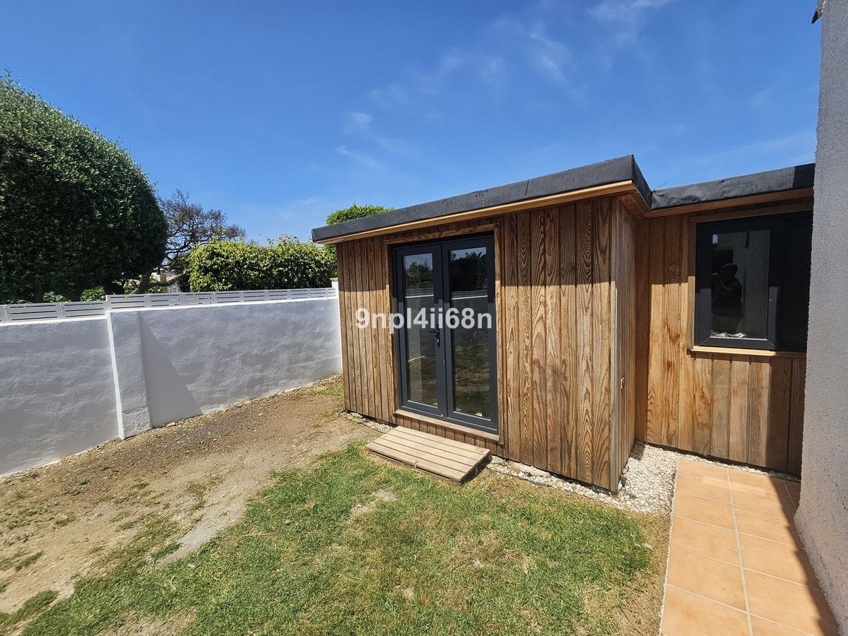 Modern wooden garden room with double glass doors and a small window, set against a blue sky.