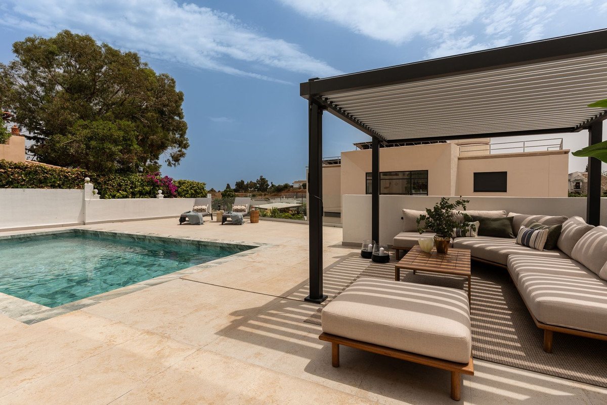 A spacious outdoor terrace with a swimming pool, lounge seating, and a pergola providing shade on a sunny day.