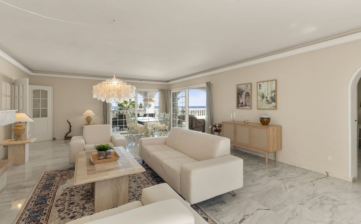 Bright living room with white sofas, marble floors, and a balcony offering a sea view.