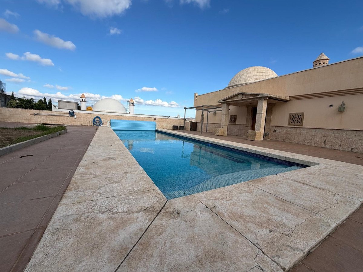 A large swimming pool with a covered section sits beside a building with domed roofs and an outdoor terrace.