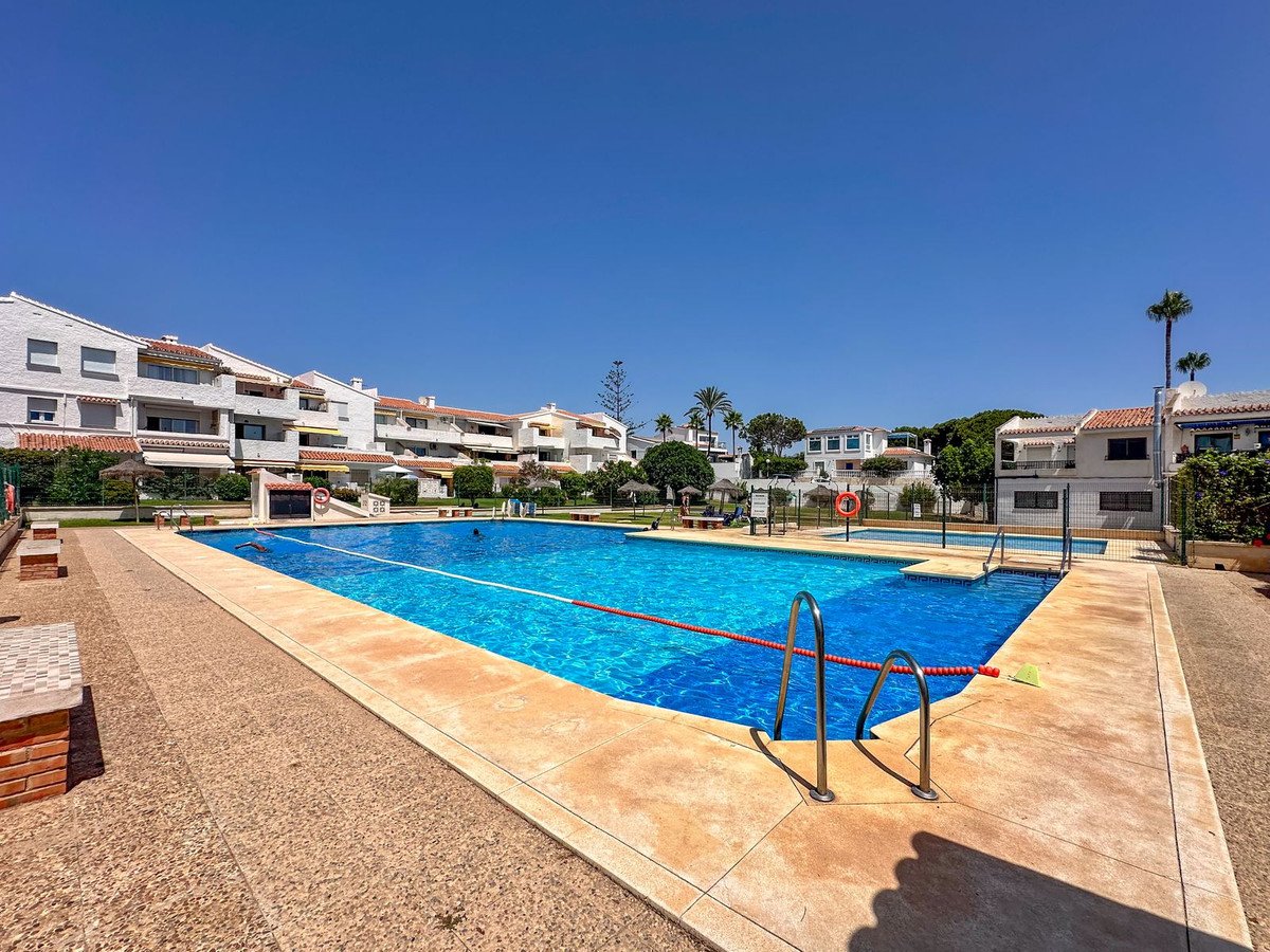 Large outdoor swimming pool with crystal blue water, surrounded by apartments and palm trees under a clear blue sky.