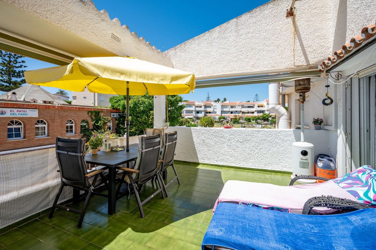 Sunny terrace with dining table, chairs, yellow umbrella, and a view of residential buildings and greenery.