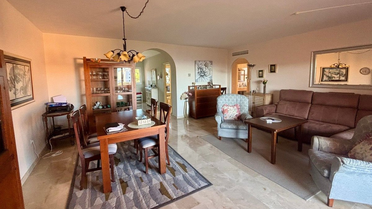 Open plan living and dining room with brown sofa, wooden table, and arched doorways