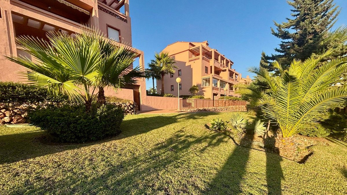 Apartment complex with lush garden and palm trees under sunny sky