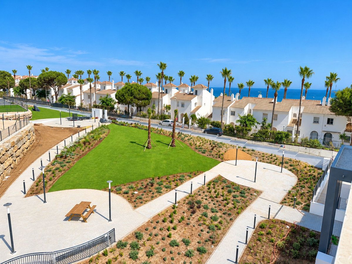 Modern residential complex with white houses, palm trees, manicured lawns, and a picnic area with a view of the sea.