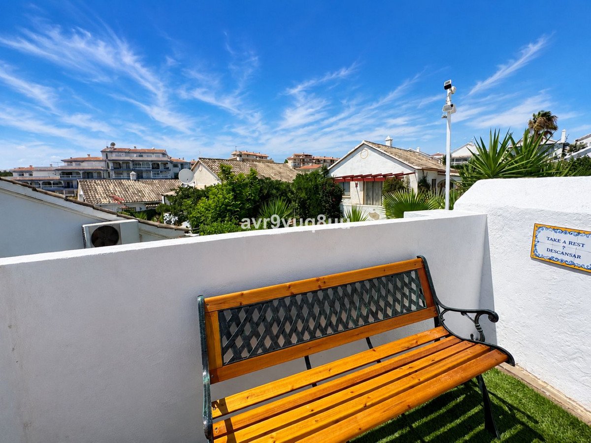 A wooden bench on a white terrace with a view of rooftops and a blue sky.
