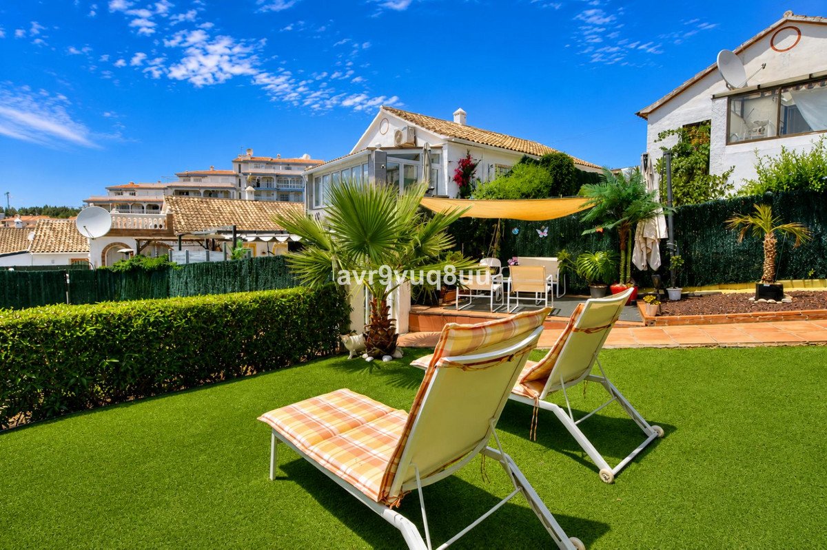 Garden with green lawn, lounge chairs, dining set, and a palm tree under a sunny sky with blue clouds.