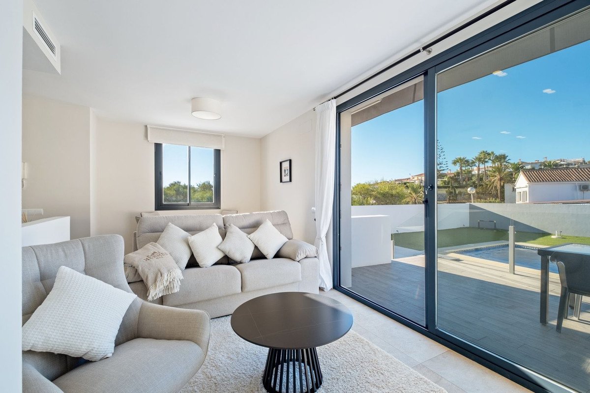 Bright living room with sofa, armchair, coffee table, and large sliding doors opening to a terrace with a pool and garden.