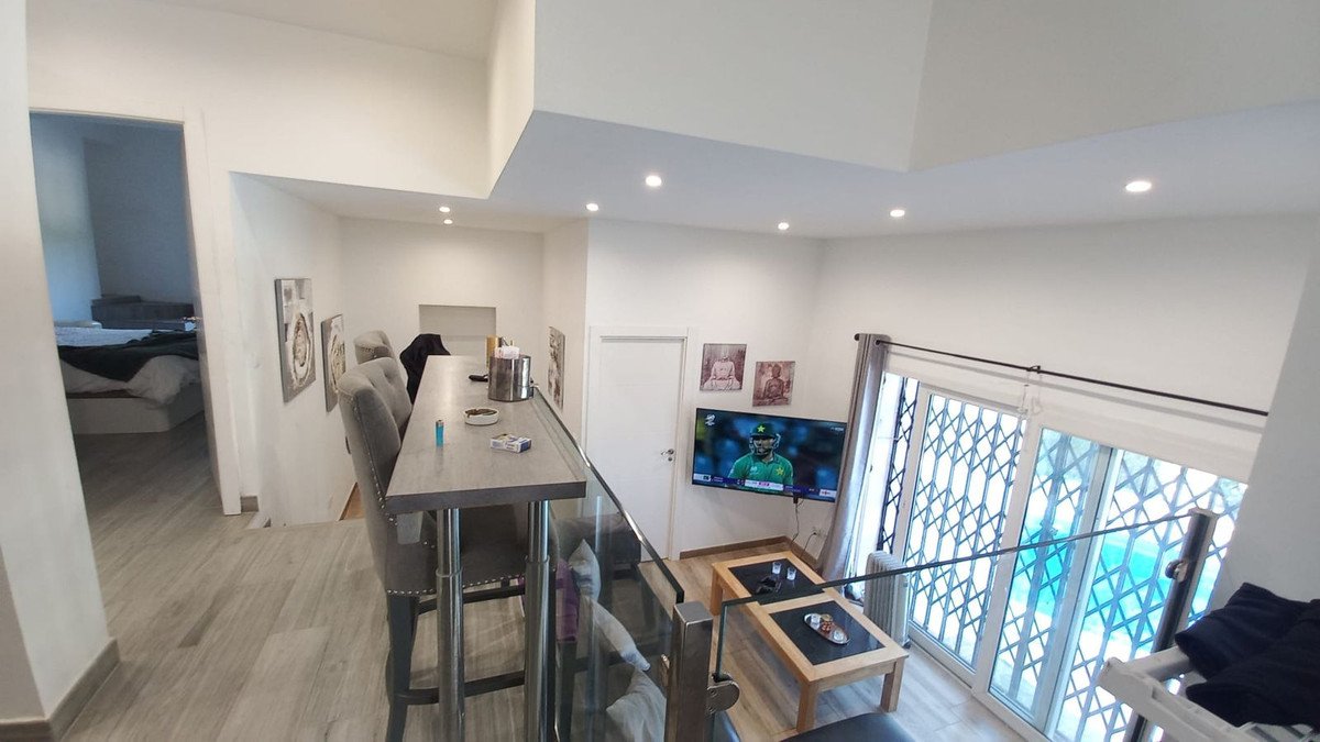 Modern living room with a bar, high chairs, coffee table, TV, and a view into a bedroom.