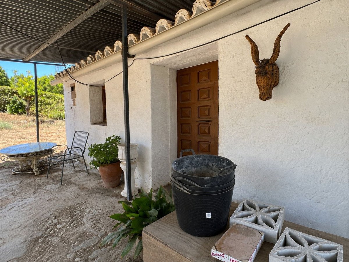 Outdoor patio with a table, chair, and potted plants next to a rustic house entrance.