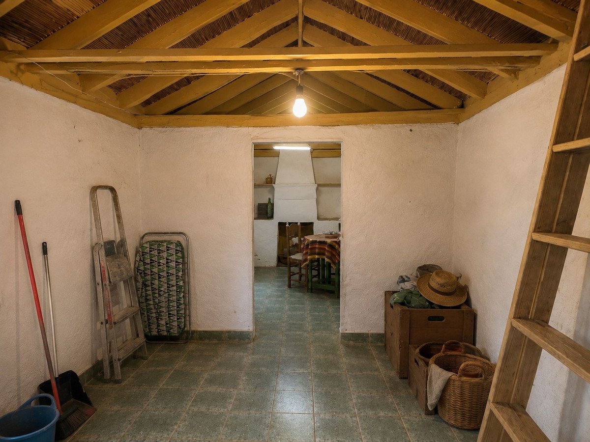 Rustic storage area with exposed wooden beams, ladder, and straw hat. View into a dining area.