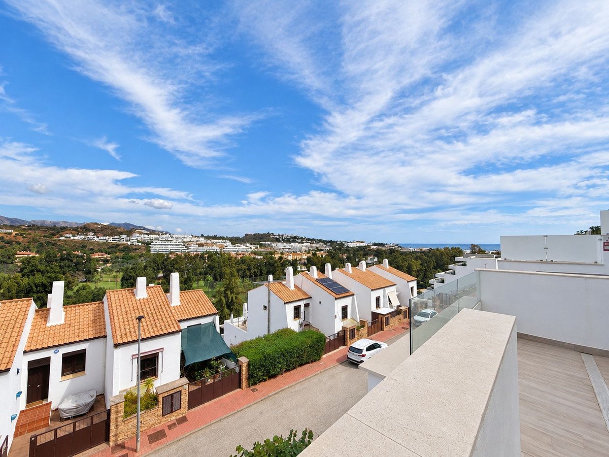 Townhouse complex with a terrace offering panoramic views of the sea, hills, and surrounding greenery under a blue sky with clouds.