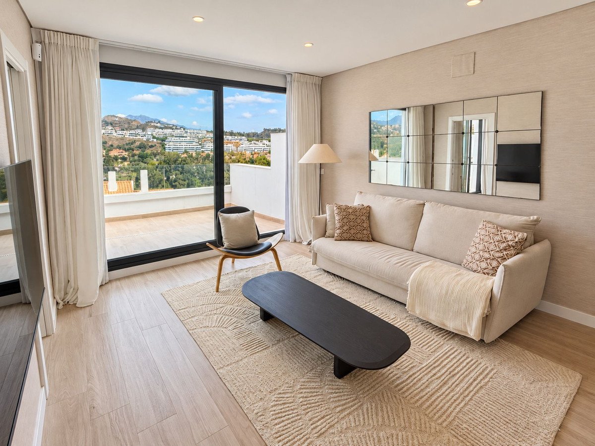 Living room with a sofa, modern coffee table, and a large window offering a view of the sea and hills.