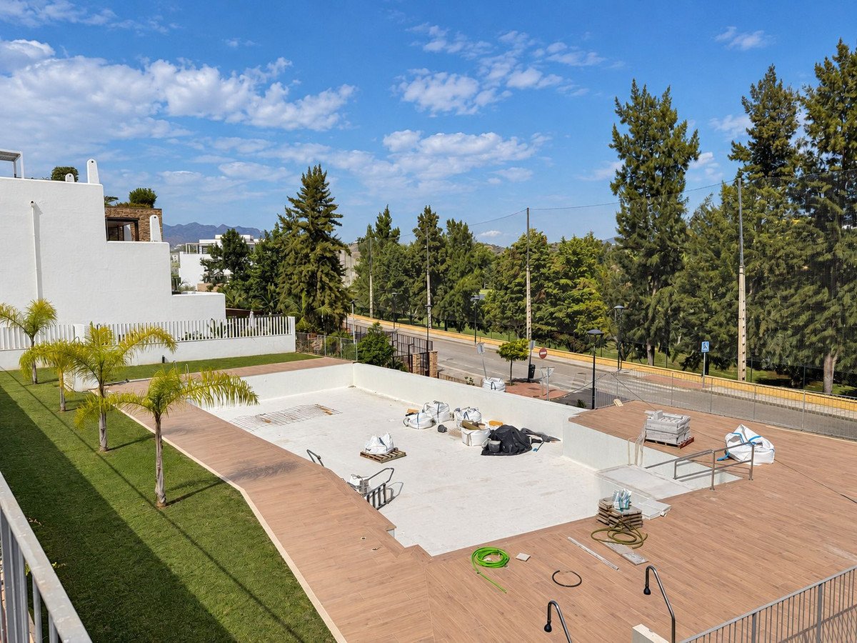 Outdoor area with an unfinished pool, wooden decking, palm trees, and green lawn, under a partly cloudy sky.