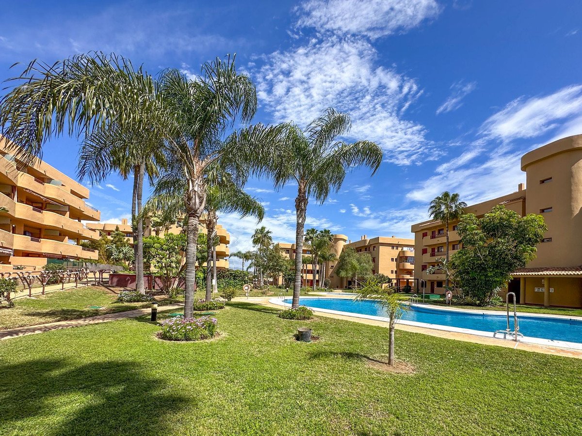 Apartment complex with swimming pool, palm trees, and green lawns under blue sky