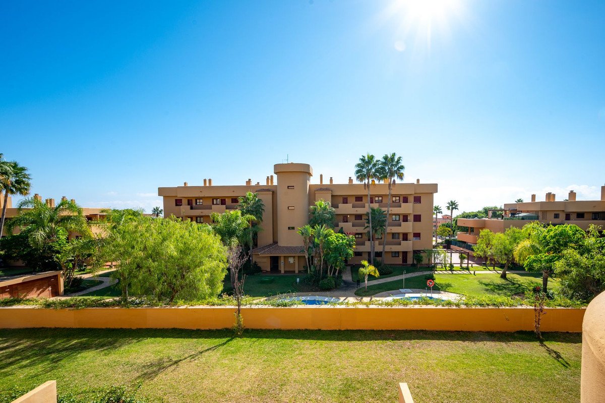 View of a sunny apartment complex with a pool and lush greenery