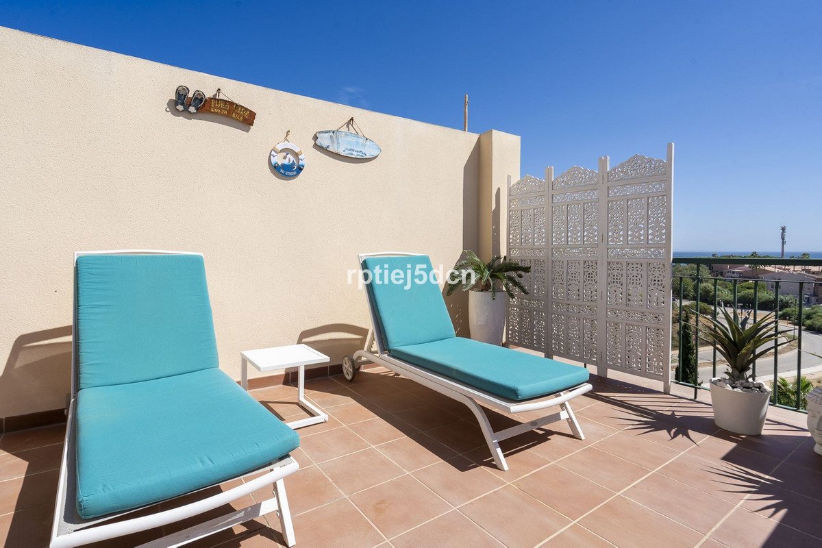 Two turquoise lounge chairs on a tiled terrace with sea view, decorated with beach-themed wall art and a white folding screen.