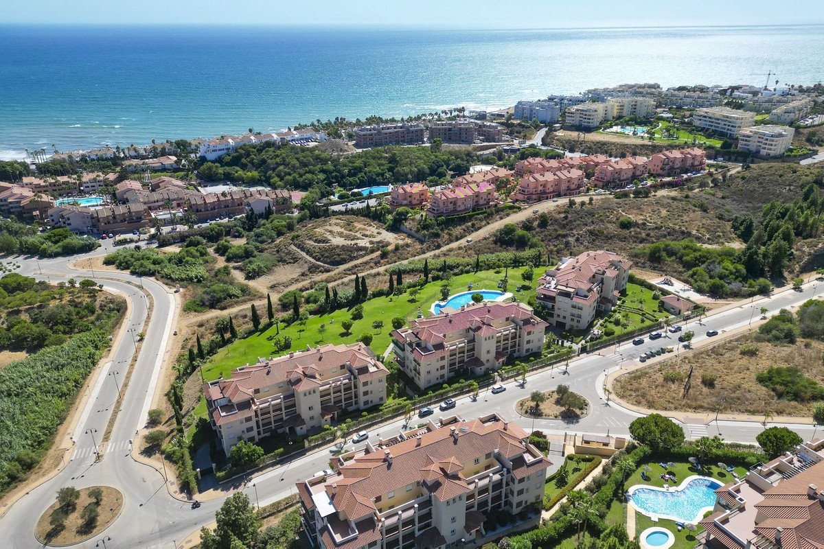Aerial view of resort buildings with pools and the ocean in the background, showcasing a coastal development with lush greenery.