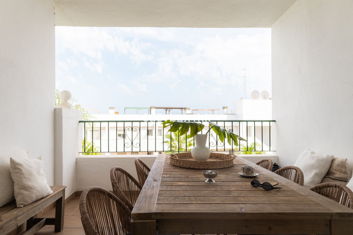 Outdoor terrace dining area with wooden table, chairs, and a view of buildings under a cloudy sky.