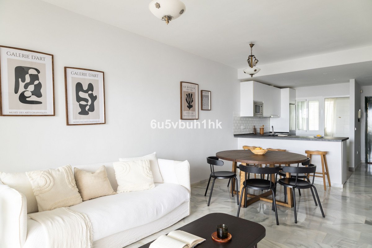 Modern living and dining area with a white sofa, round dining table, and a sleek white kitchen with bar stools.