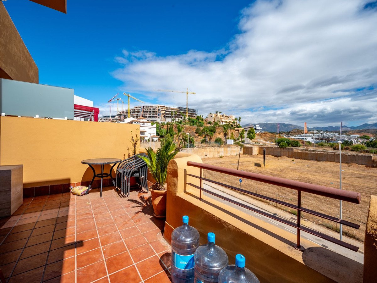 Terrace with table and chairs overlooking an area with construction and distant hills under a blue sky.