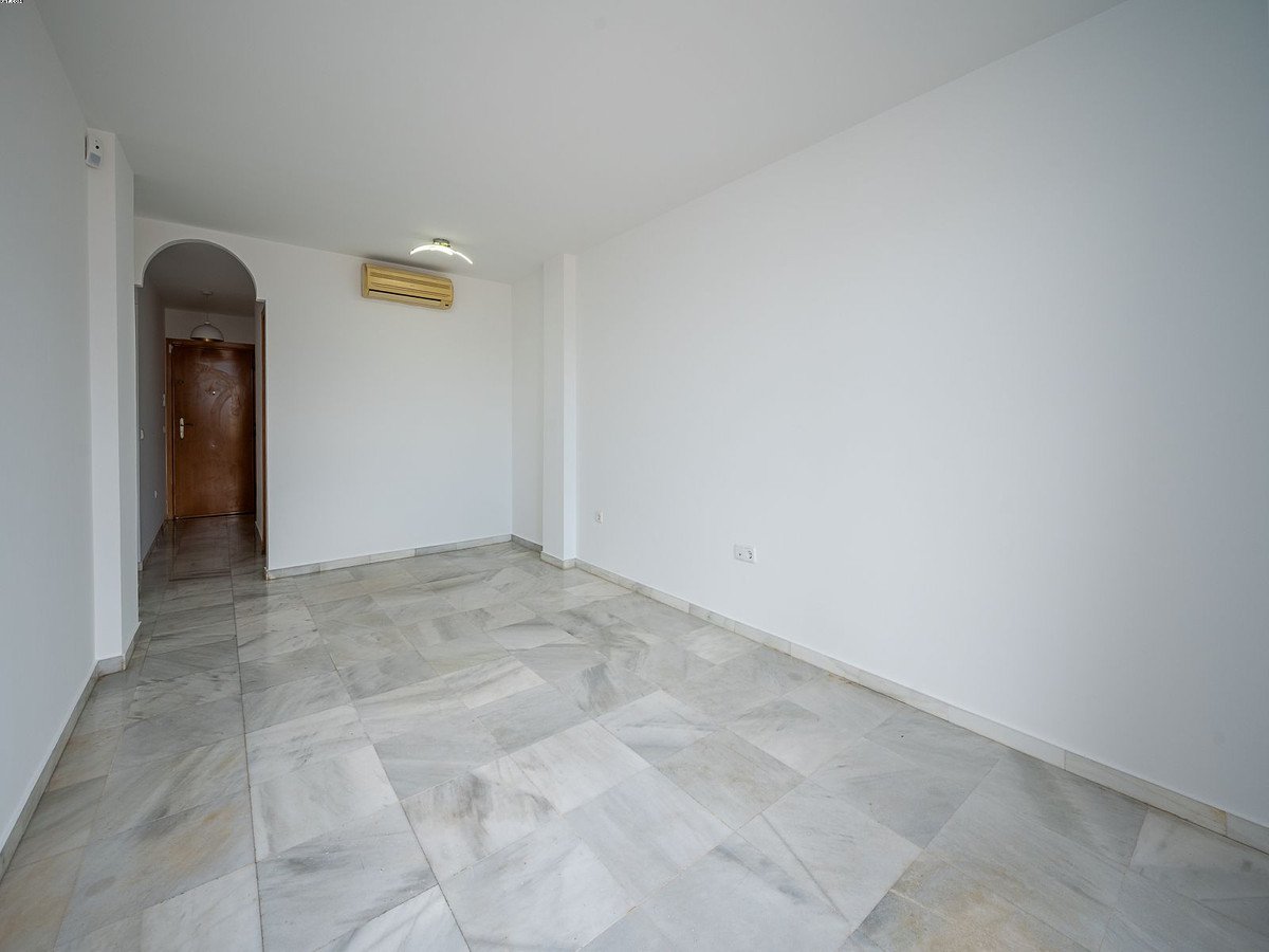 Empty living room with white walls, marble floors, and an air conditioning unit on the wall near a doorway.