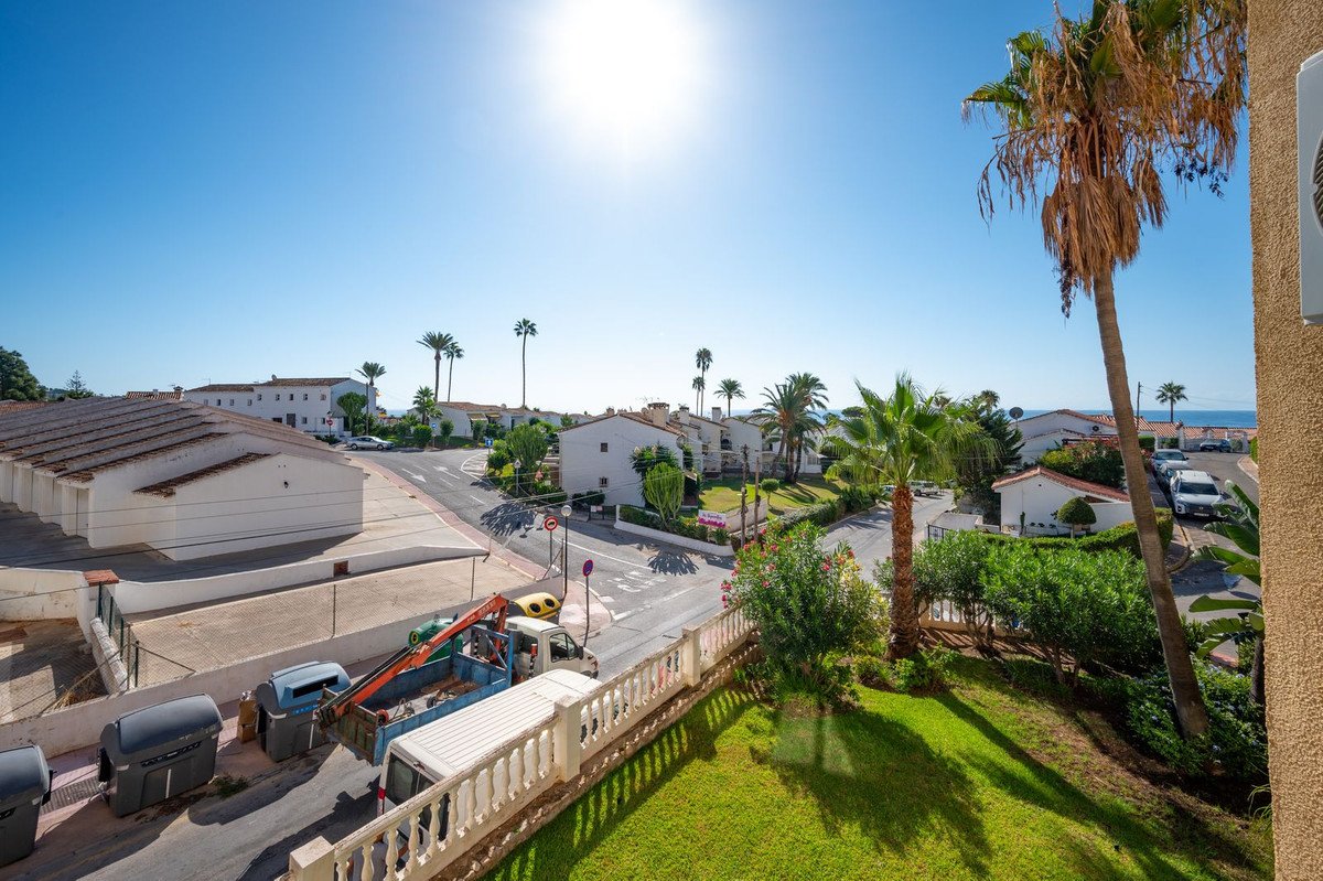 View from a balcony overlooking palm trees, white houses, and the sea under a bright blue sky.
