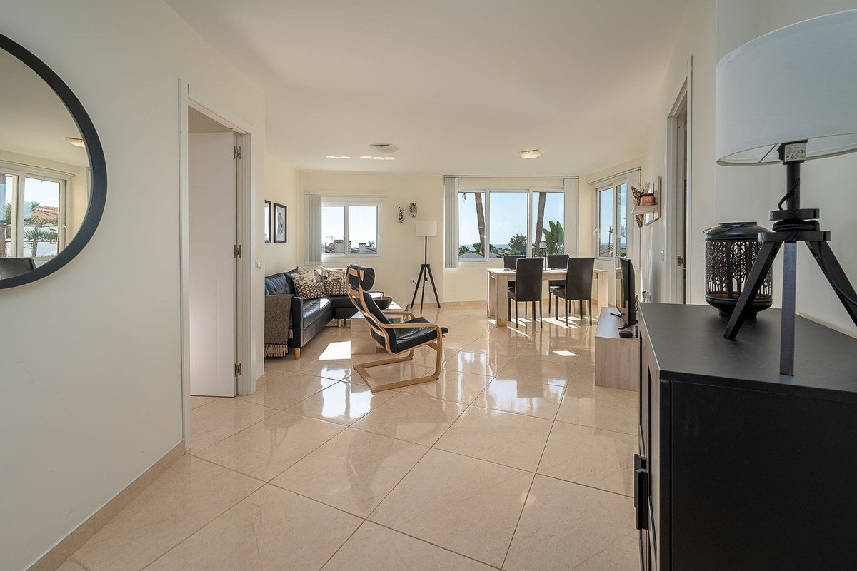 Spacious living and dining area with a black leather sofa, chairs, and a table overlooking the sea.