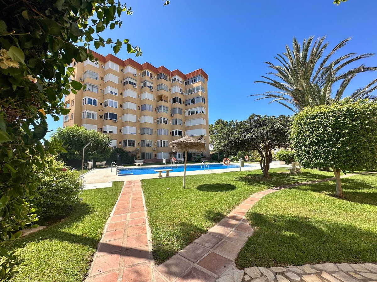 Apartment building with swimming pool and manicured gardens on a sunny day.