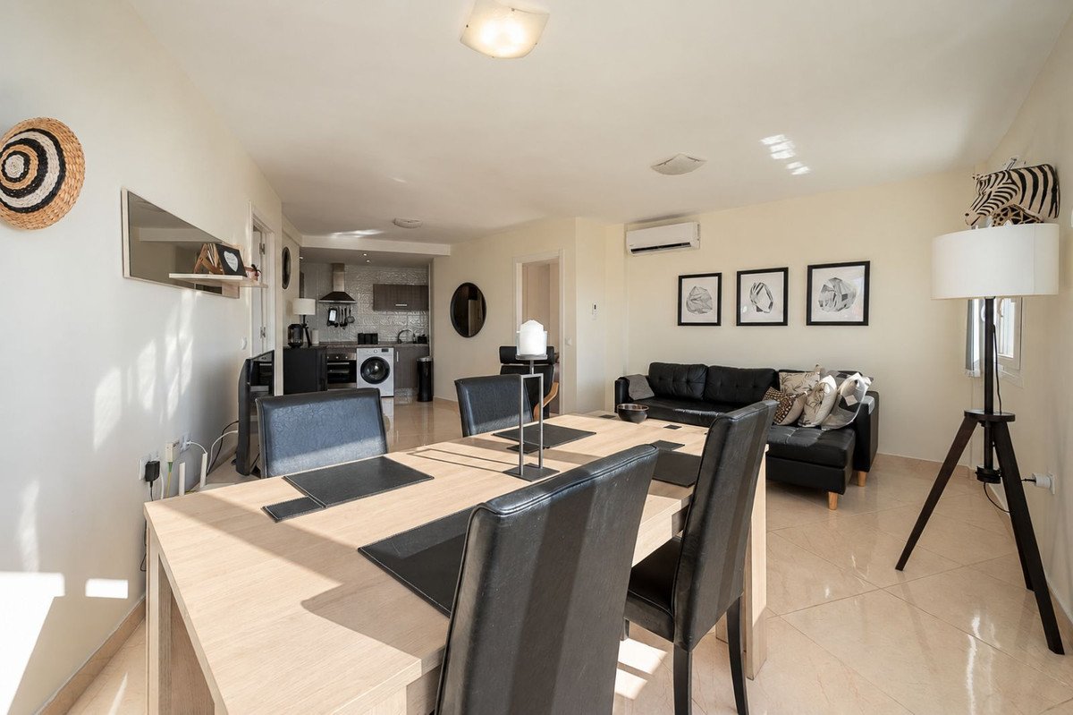 Modern open-plan living and dining area with a black leather sofa and kitchen in the background. Bright and airy.