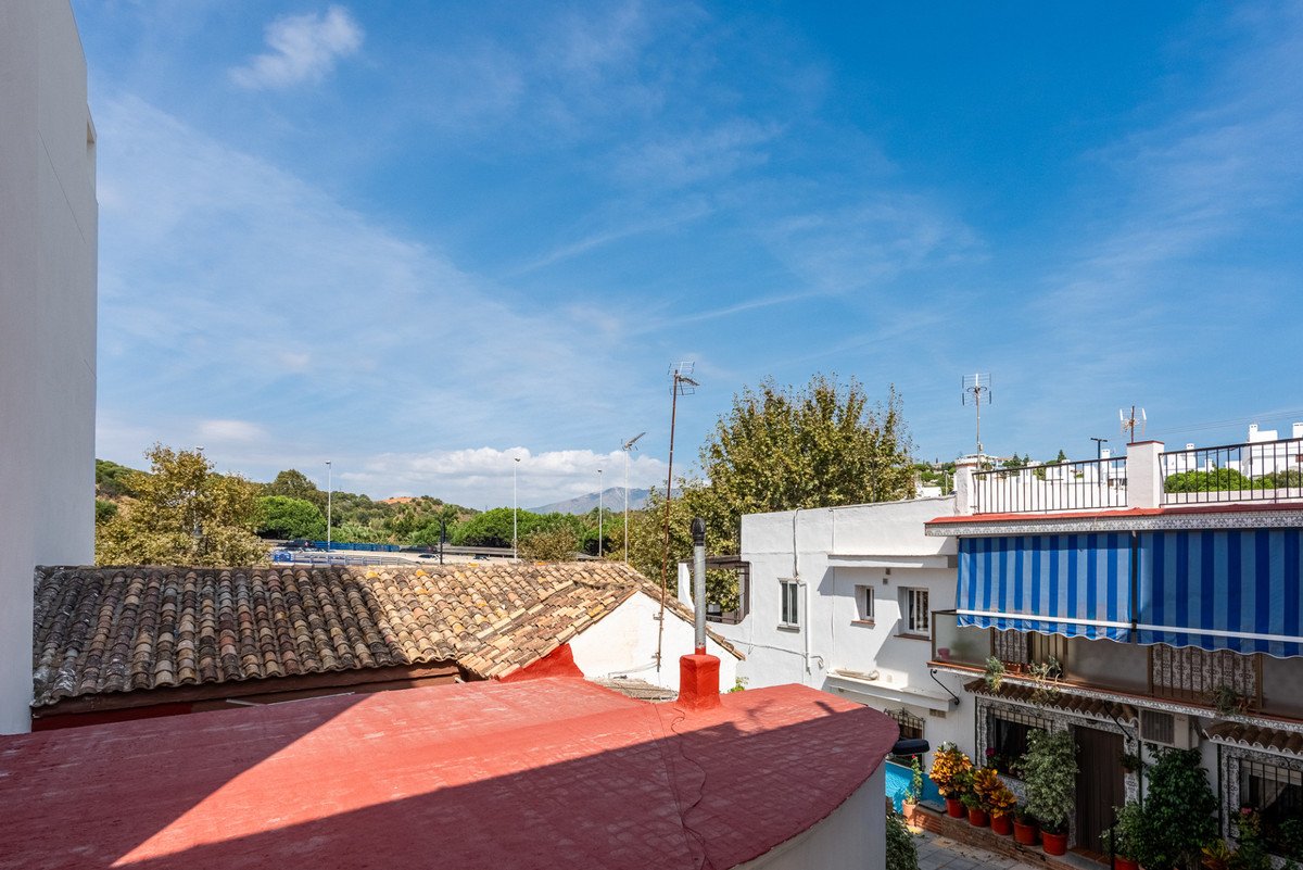 View of rooftops, trees, and blue sky with clouds from a balcony.