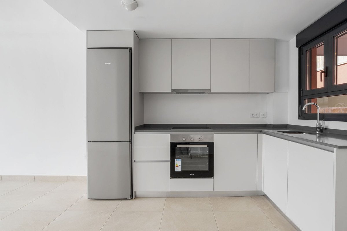 Modern L-shaped kitchen with sleek white cabinets, integrated oven, induction hob, and a stainless steel refrigerator.