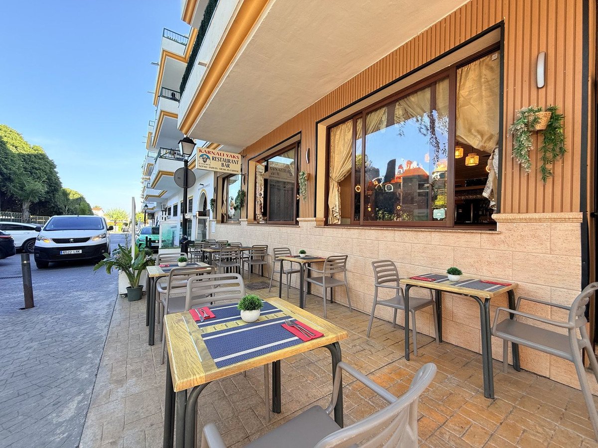 Outdoor seating area of a restaurant with tables and chairs set up on the sidewalk with a view of the street.