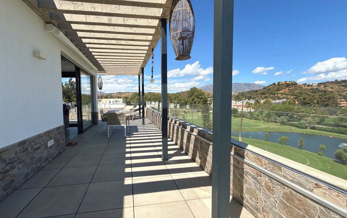 Modern terrace with golf course and lake view, featuring outdoor dining furniture and a shaded pergola overhead.