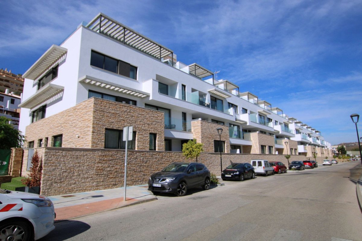 Modern townhouse complex with white facades, stone base, balconies, and rooftop terraces under a blue sky.