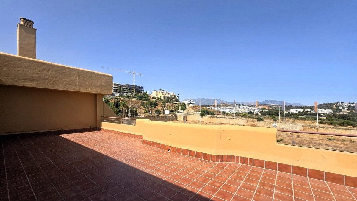 Spacious tiled terrace with a chimney and a distant view of buildings, mountains, and a clear blue sky.