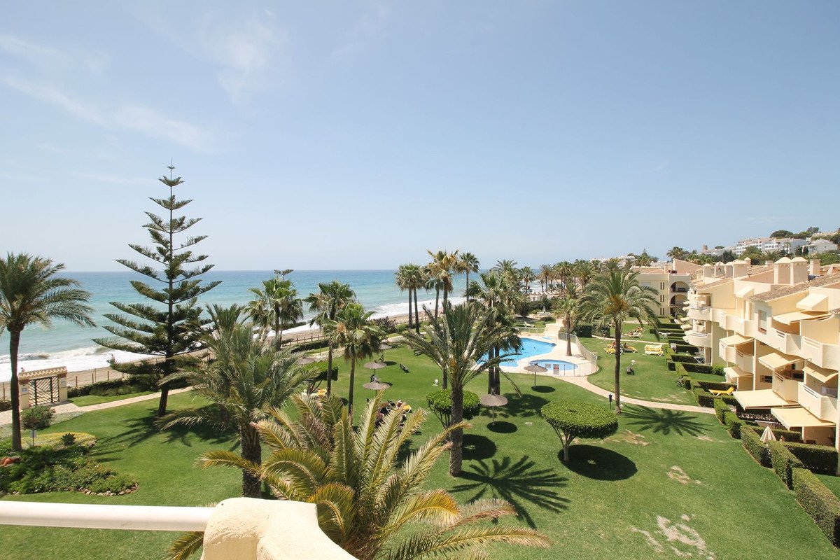 Balcony view of beach, palm trees, pool, and apartment buildings
