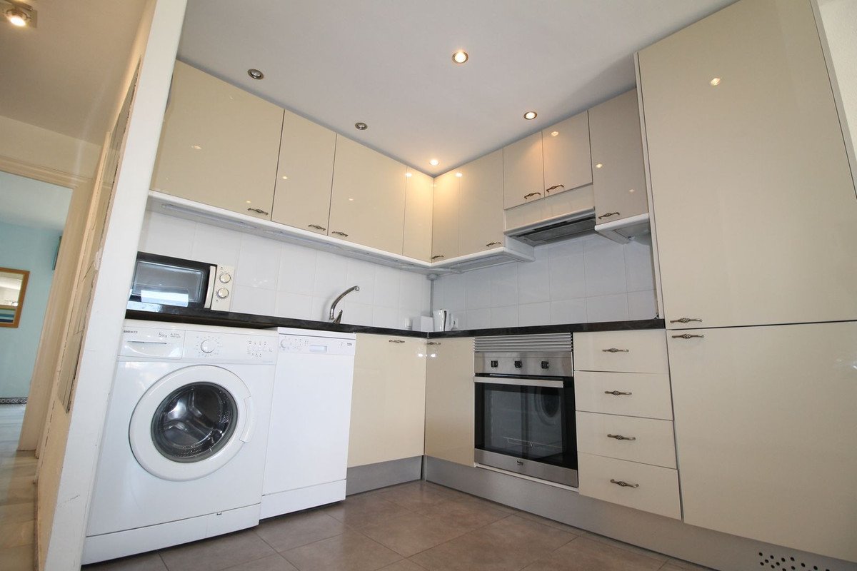 Modern kitchen with white cabinets, washing machine, and built-in oven