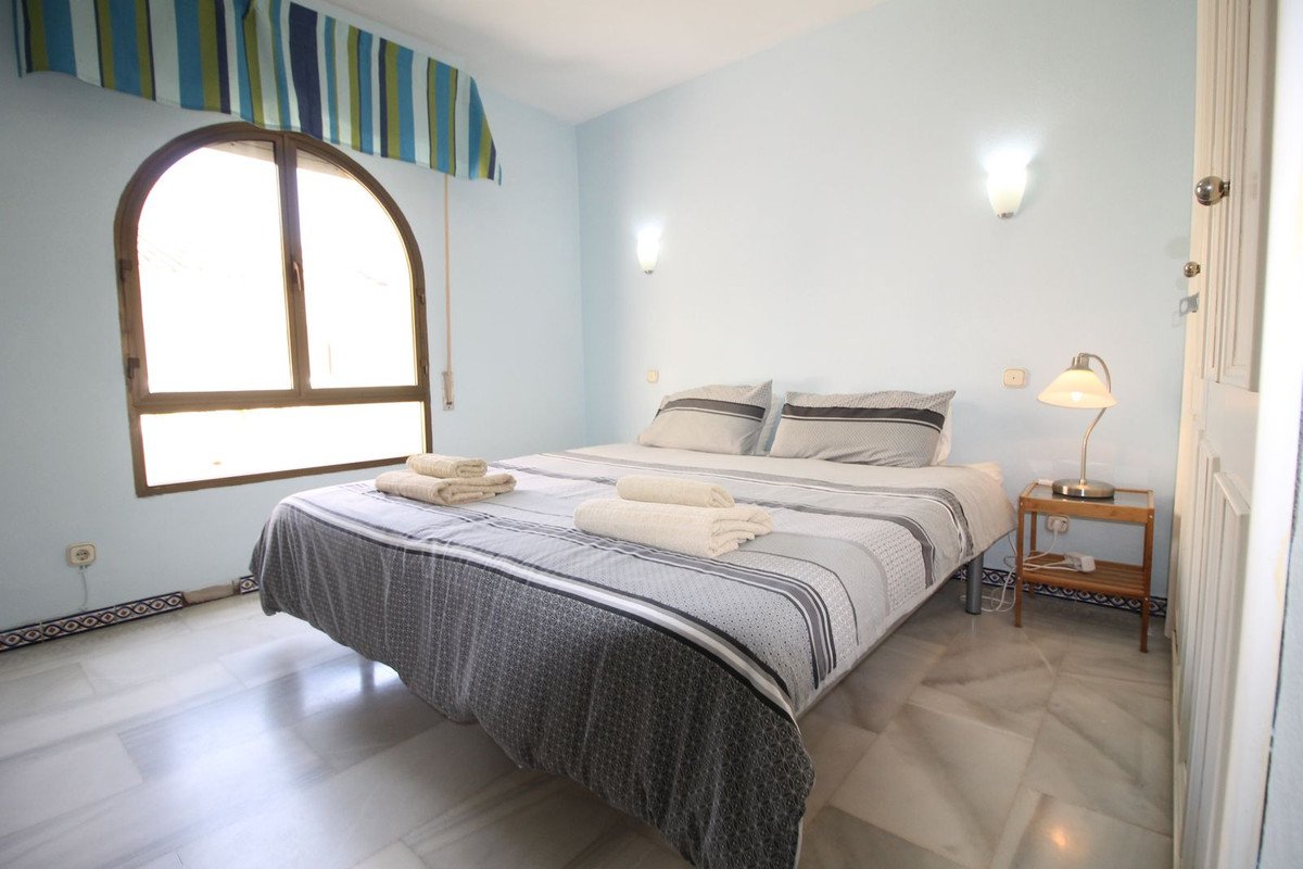 A bright bedroom with light blue walls, a large bed, and an arched window.