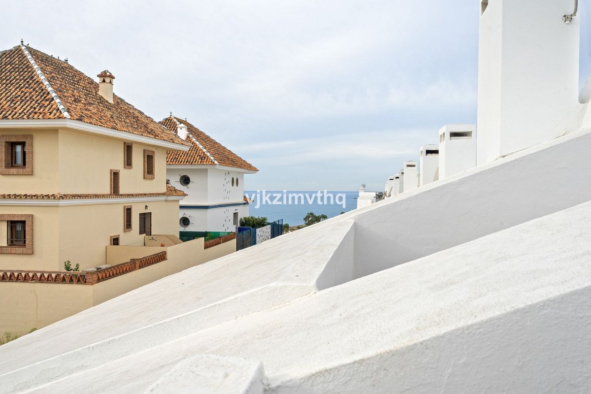 View of the sea and houses from a white tiled terrace with multiple chimneys in the foreground.