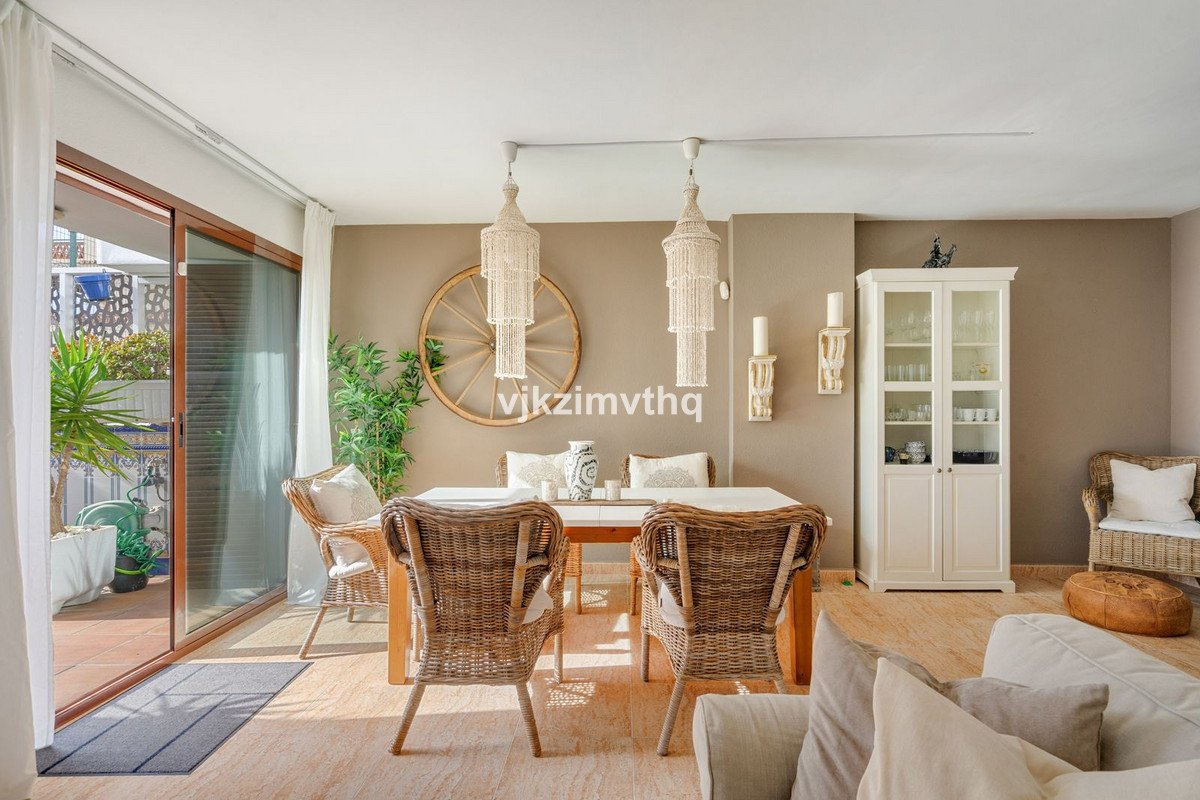 A bright dining area with a table, chairs, and a cabinet, opening onto a sunny terrace with plants.