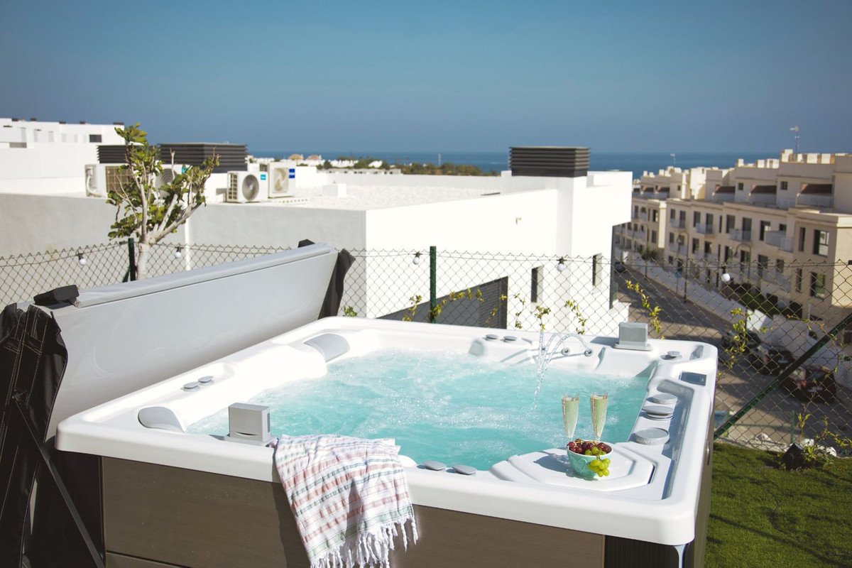 Outdoor jacuzzi with bubbling water, champagne flutes, and grapes, offering a view of the sea and buildings.