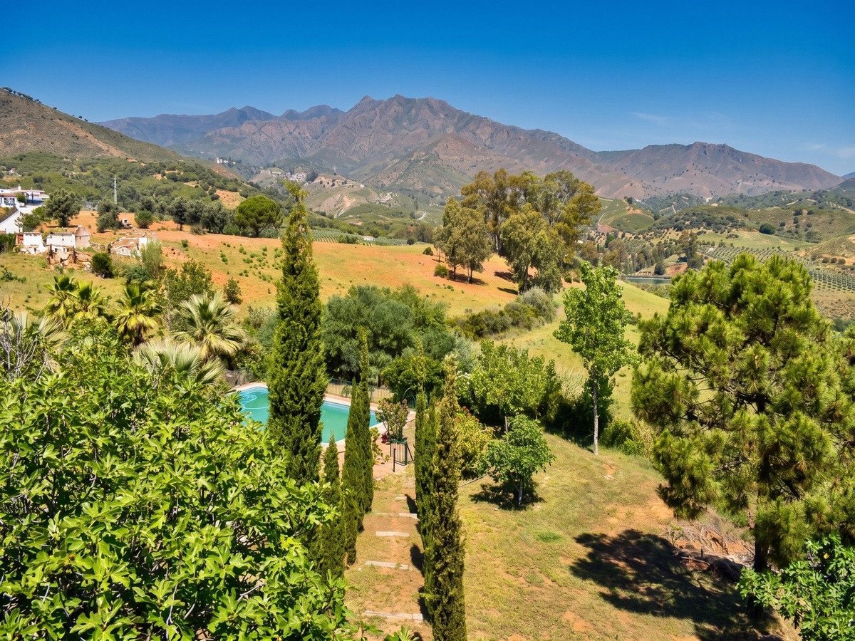 A beautiful countryside landscape with a swimming pool, lush greenery, and majestic mountains in the background under a clear blue sky.