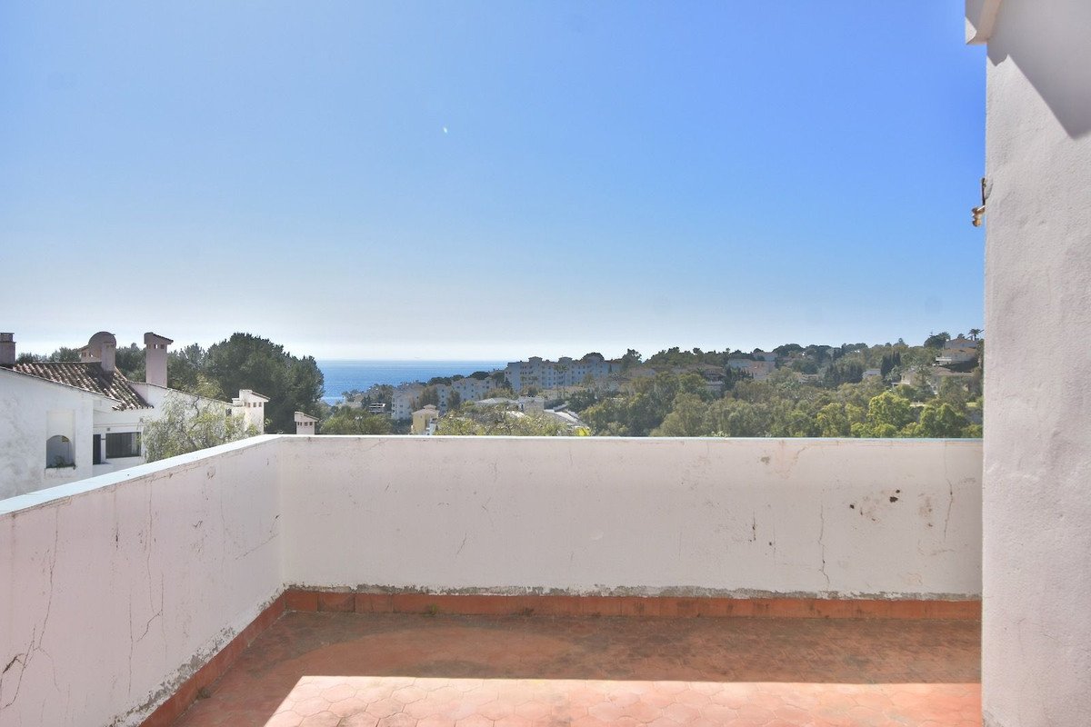 Terrace with a clear blue sky and a distant view of the sea, overlooking a residential area with trees.