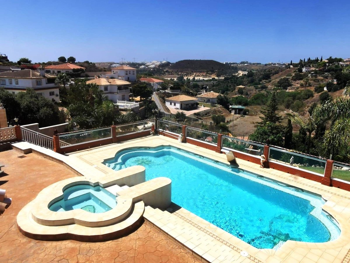 Luxury swimming pool and jacuzzi with a view of the rolling hills and surrounding houses under a clear blue sky.