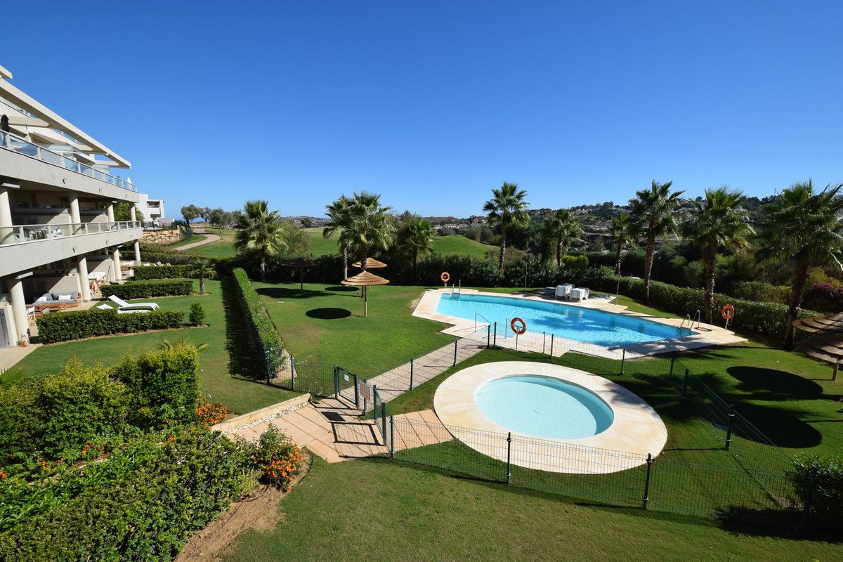 Modern apartment complex with balconies overlooking a swimming pool, jacuzzi, lush gardens, and a golf course.