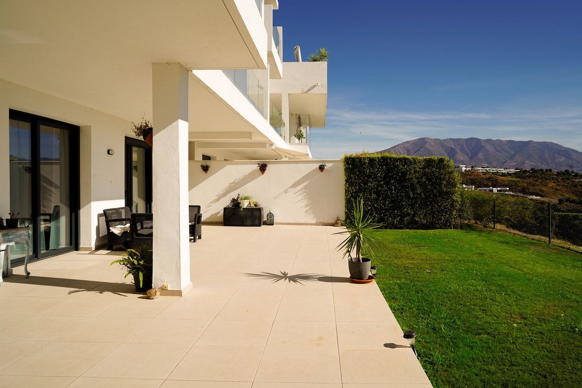Modern terrace with seating and a manicured lawn offering stunning views of rolling hills and mountains under a clear blue sky.