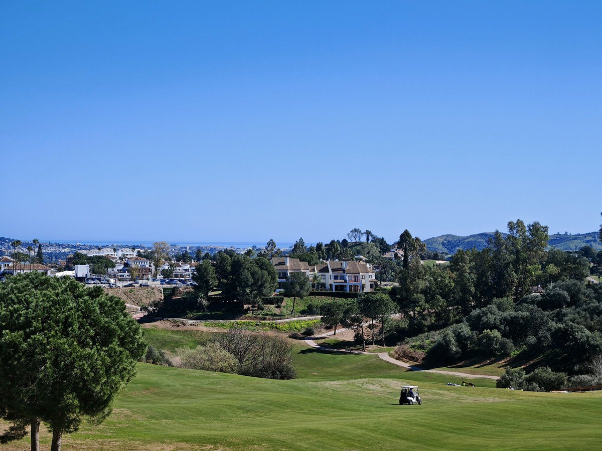 A scenic view of a golf course with a villa in the background and the sea in the distance under a clear blue sky.
