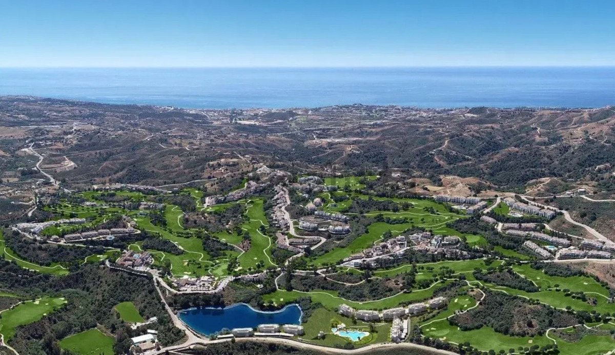 Aerial view of a luxury golf resort community with buildings, a lake, and the sea in the background.